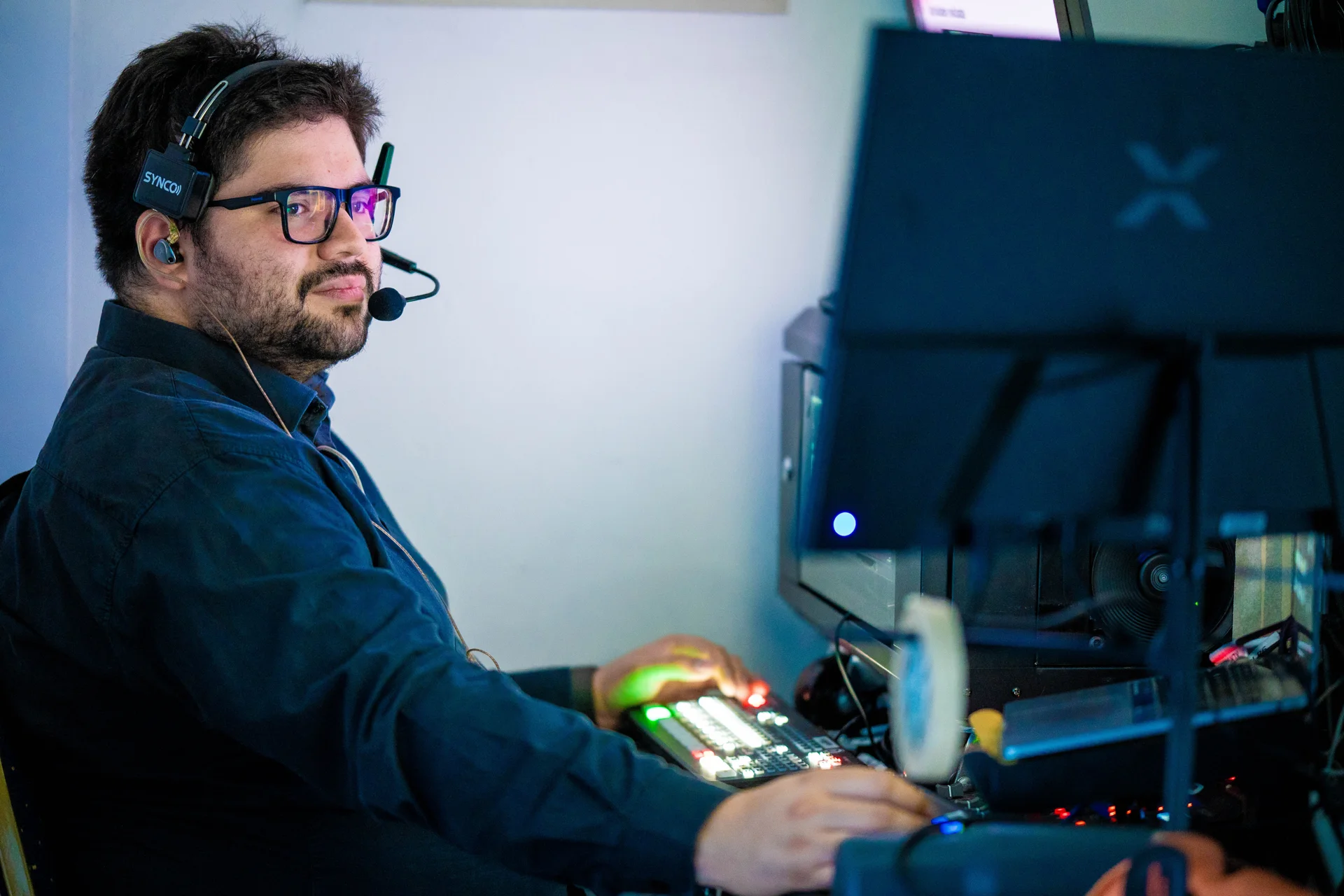 Operador con auricular de intercomunicación frente a una mesa de control audiovisual